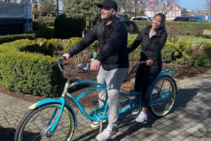 Two people riding a blue tandem bicycle on a sunny day in a park.