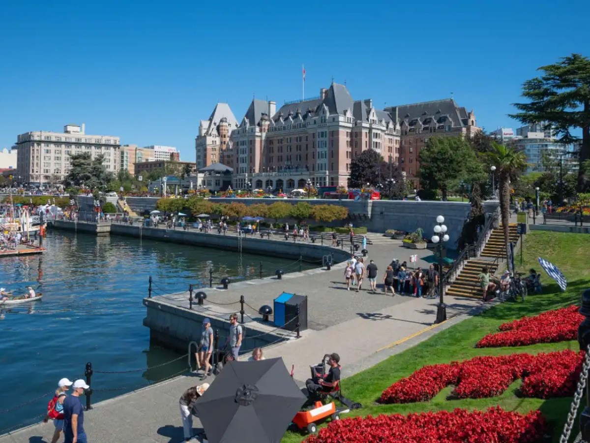 Scenic view of harbor, historic hotel, and people enjoying a sunny day in a park with flowers.