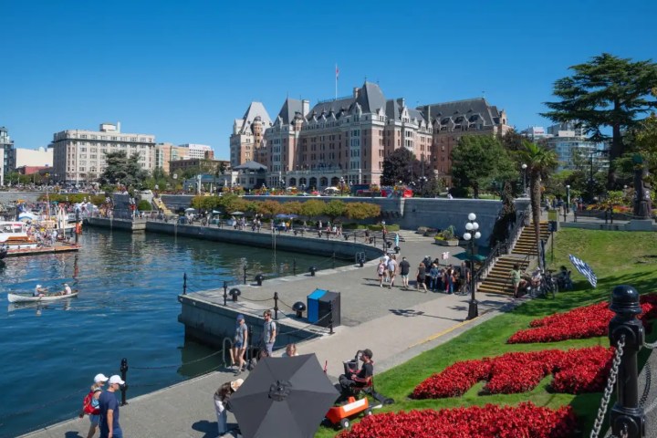 Scenic view of harbor, historic hotel, and people enjoying a sunny day in a park with flowers.